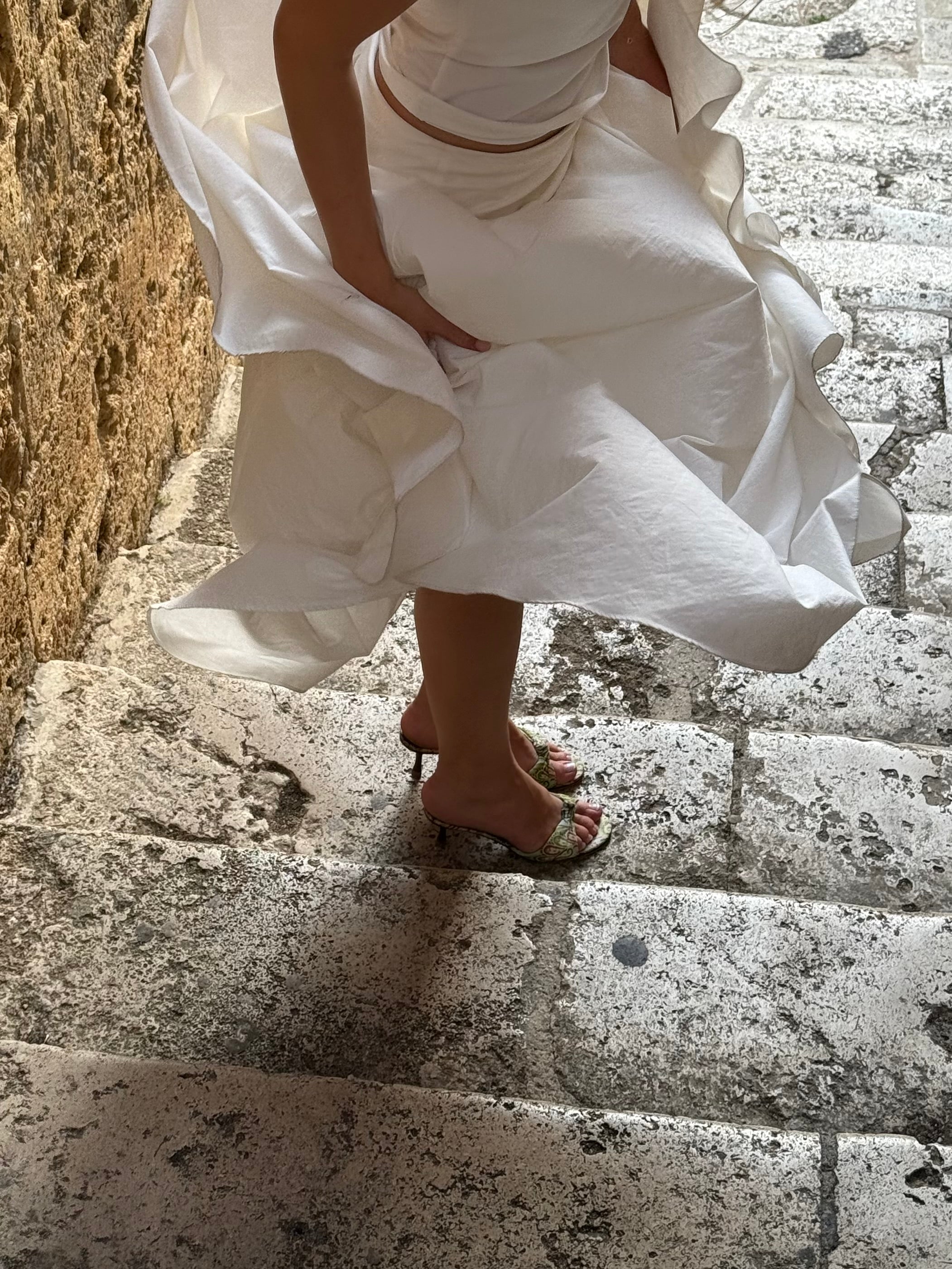 Person wearing a white dress descending stone steps.