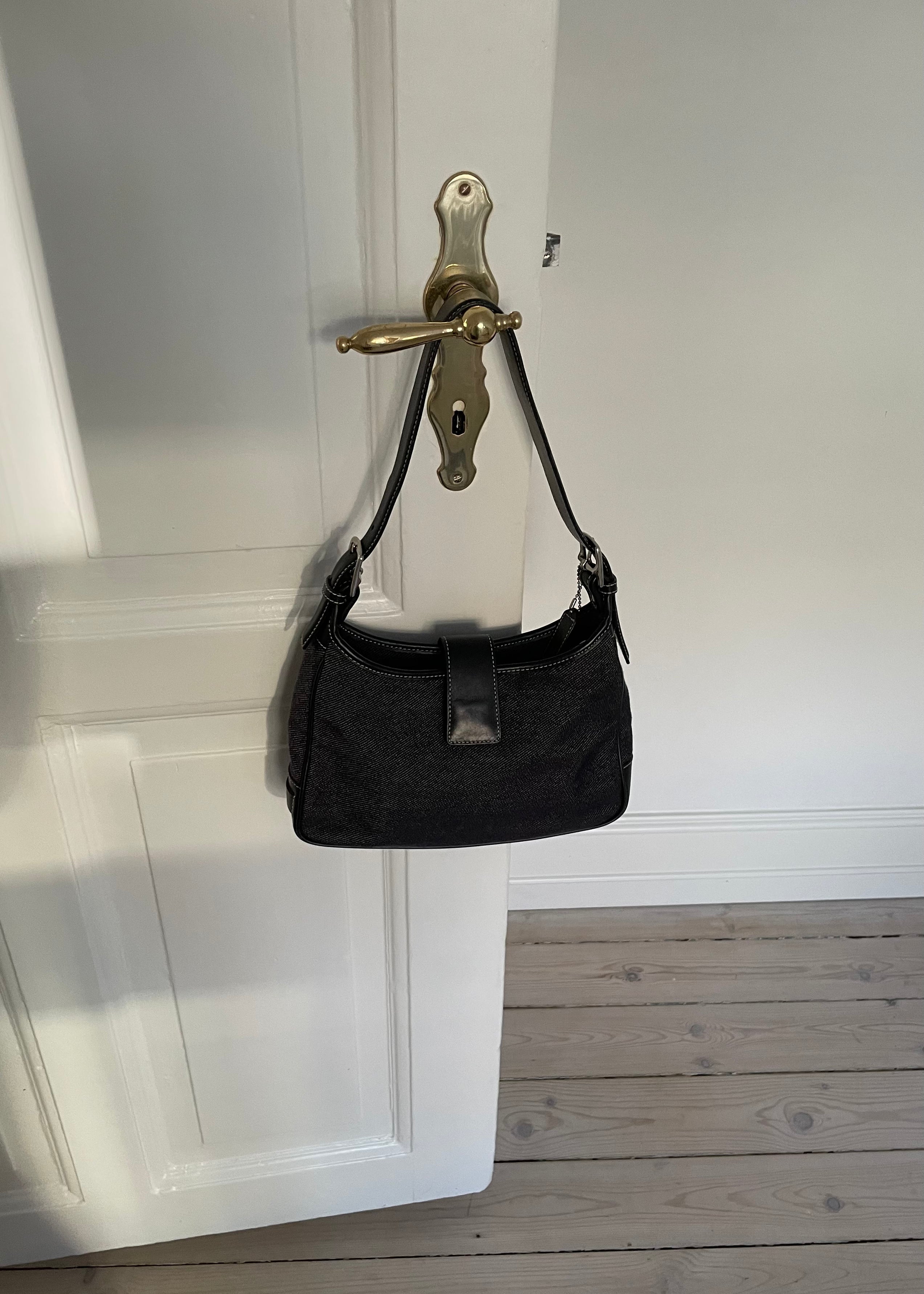 This vintage Coach bag from year 2000 is crafted from black leather and denim. It comes with an adjustable strap and magnetic closure, along with both an interior and exterior pocket. The bag is in great condition.