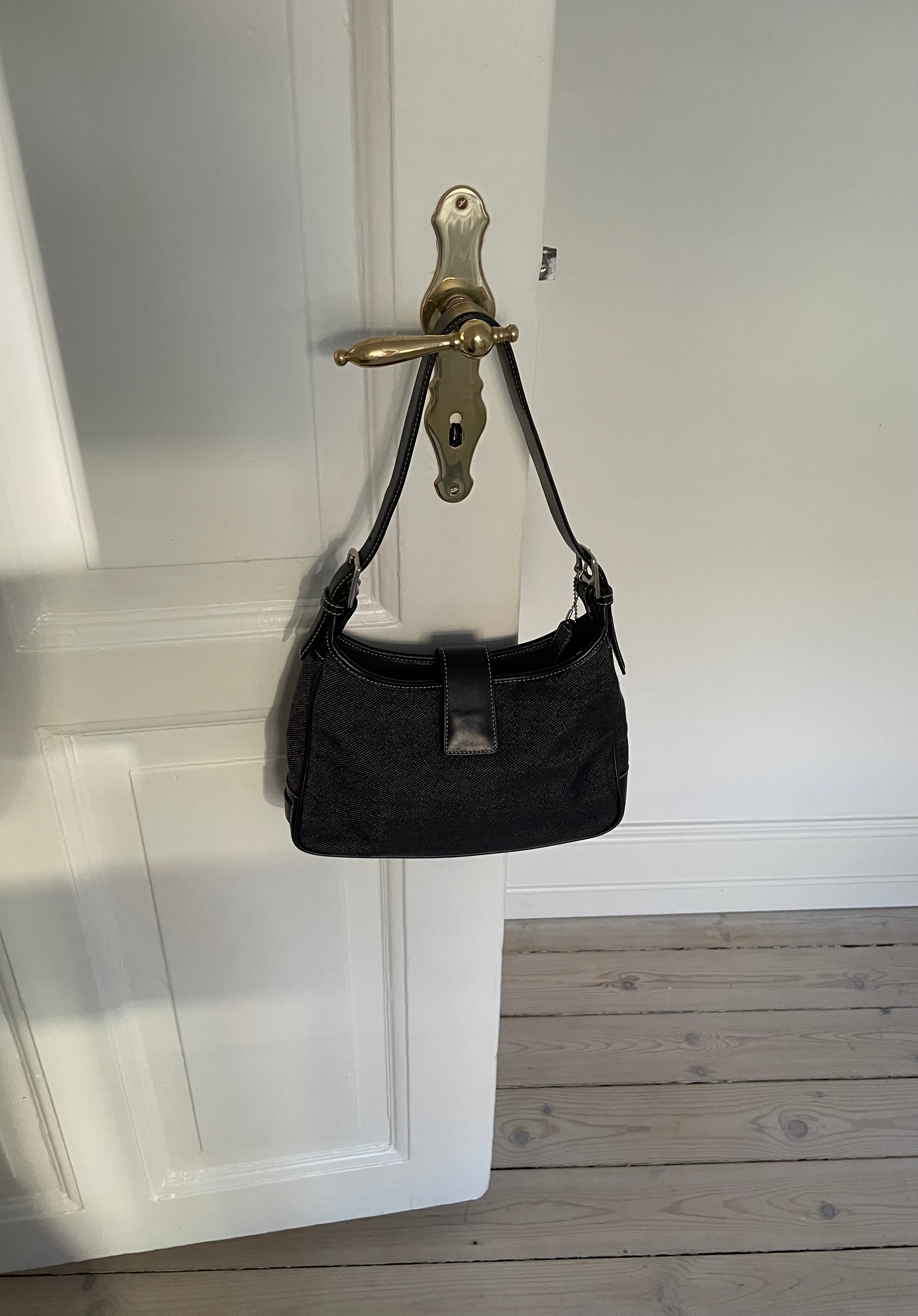 This vintage Coach bag from year 2000 is crafted from black leather and denim. It comes with an adjustable strap and magnetic closure, along with both an interior and exterior pocket. The bag is in great condition.