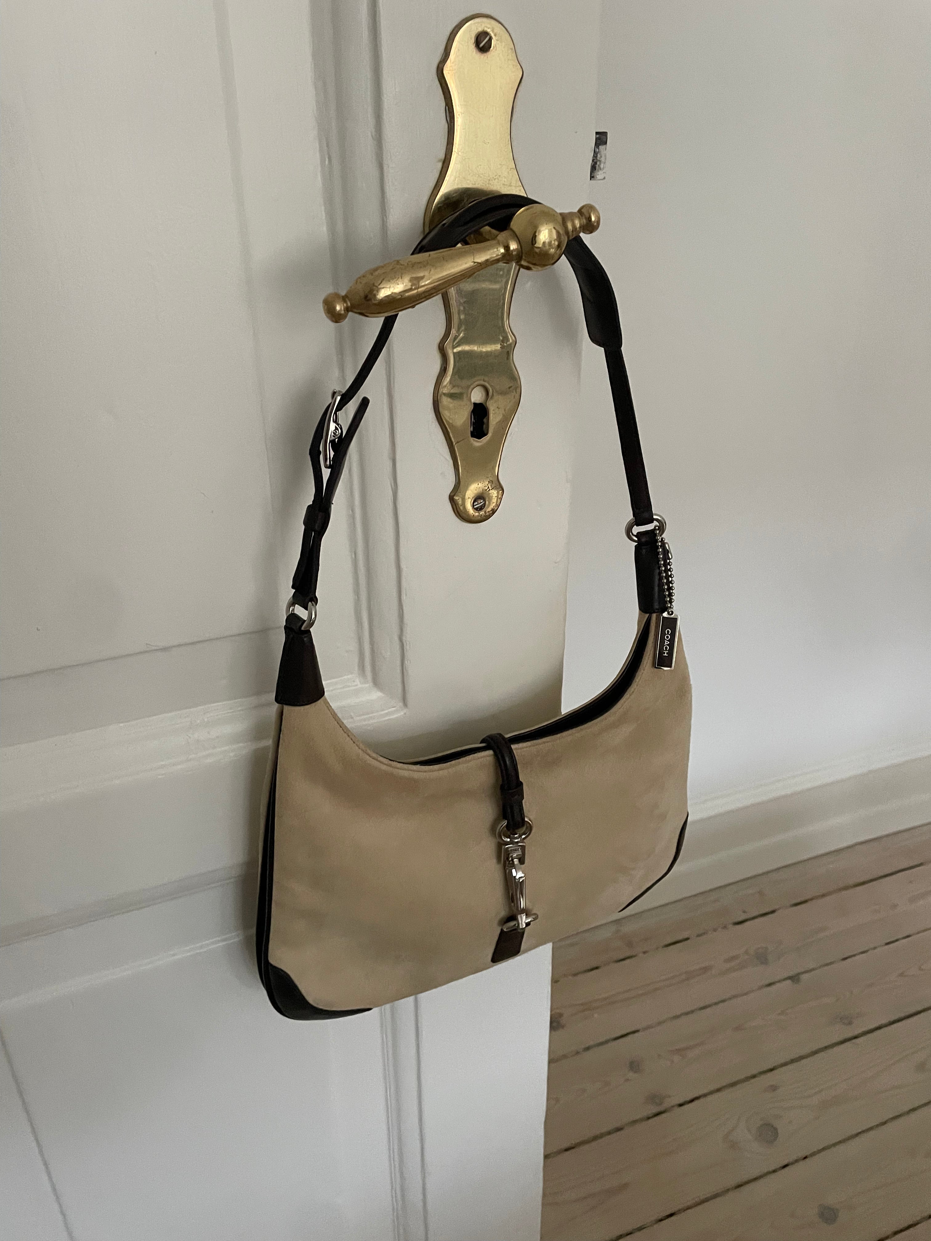 A vintage Coach shoulder bag from 2001 in beige suede with dark leather accents. The bag features a sturdy leather strap, silver-tone hardware, and a functional clasp detail on the front.&nbsp;