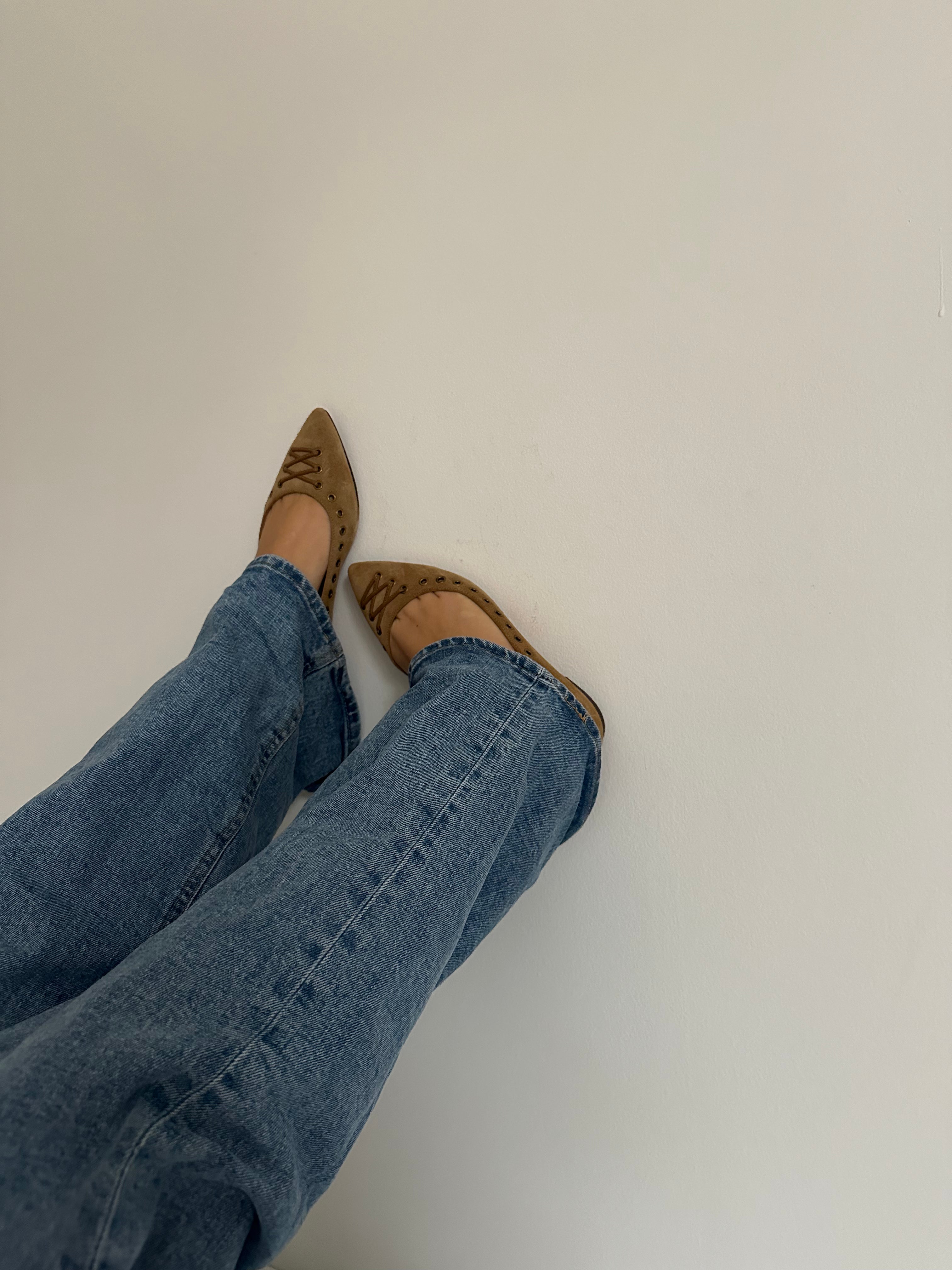 These vintage Coach ballet flats feature a pointed toe, lace-up details, and gold-tone eyelets along the edges. Crafted from beige suede with a smooth leather lining.