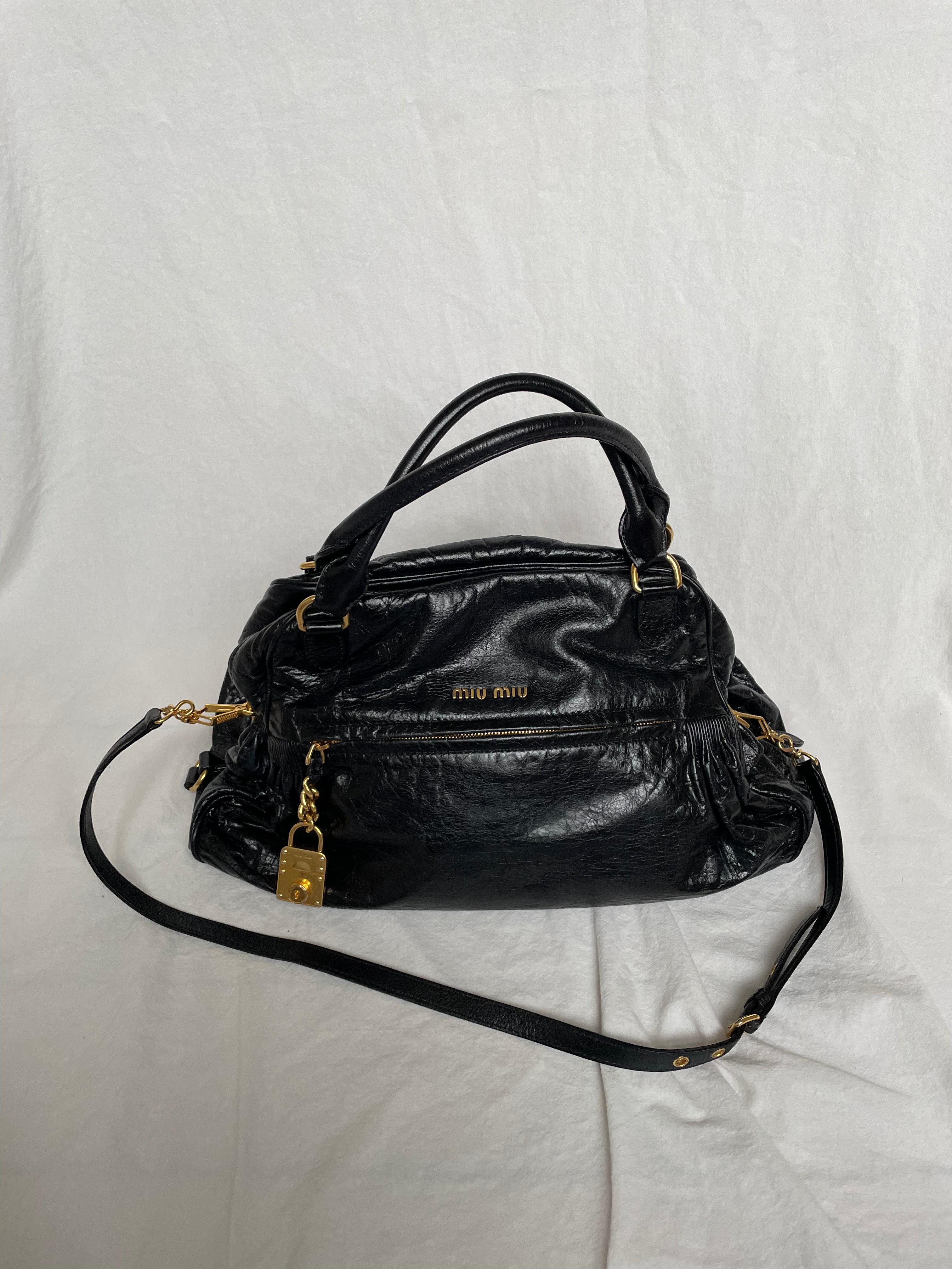 Miu Miu black nappa leather bag in a very good condition.

Crafted from nappa leather, this handbag features luxurious material and gold-tone hardware. It includes a front zip pocket, a top zip closure, and an interior slip pocket. The bag has a gold padlock charm.