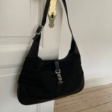 A vintage Gucci Jackie in black leather and nylon. The bag features a stylish buckle closure and a spacious interior. A timeless design perfect for any occasion.