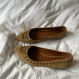 These vintage Coach ballet flats feature a pointed toe, lace-up details, and gold-tone eyelets along the edges. Crafted from beige suede with a smooth leather lining.