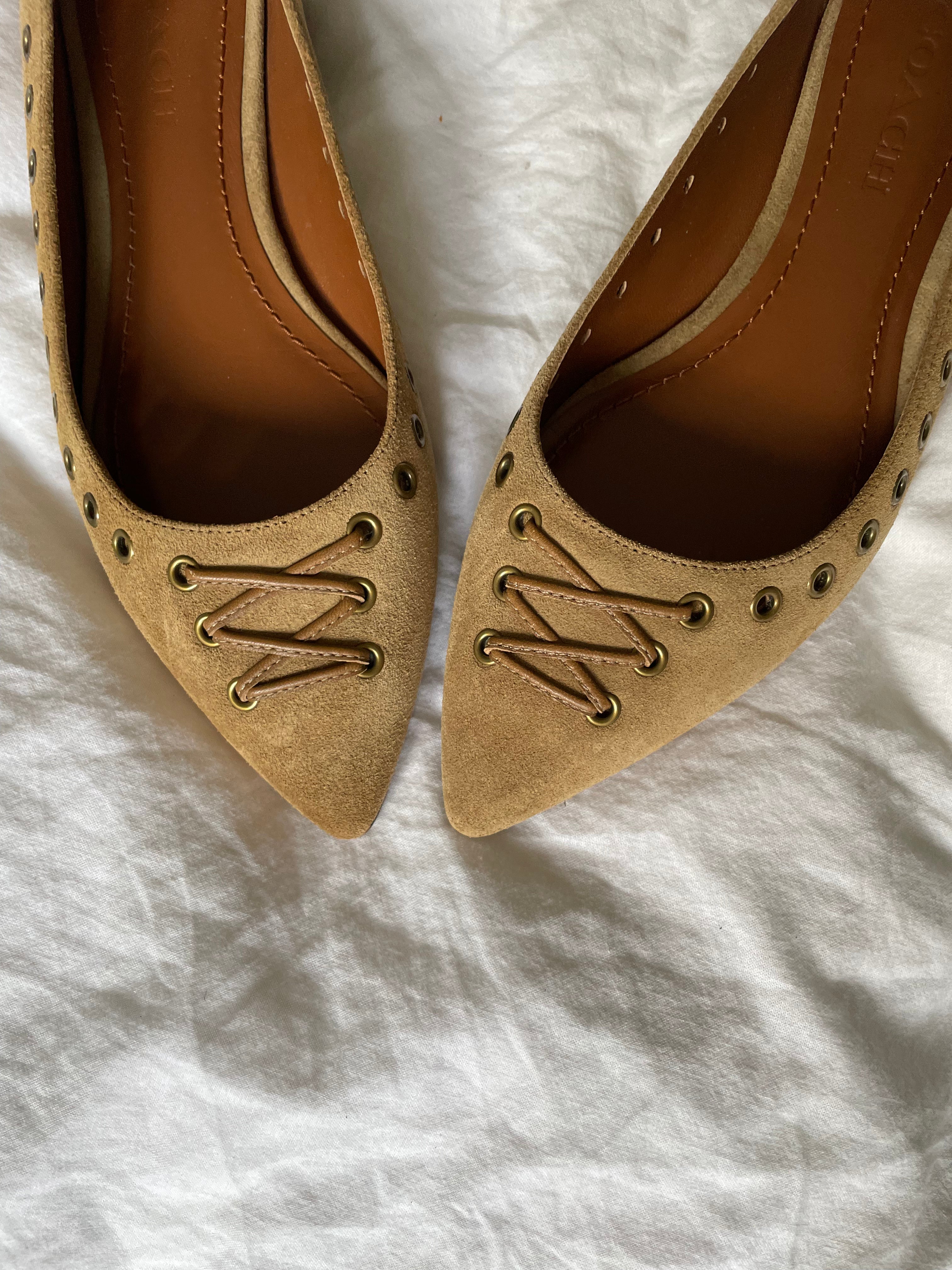 These vintage Coach ballet flats feature a pointed toe, lace-up details, and gold-tone eyelets along the edges. Crafted from beige suede with a smooth leather lining.