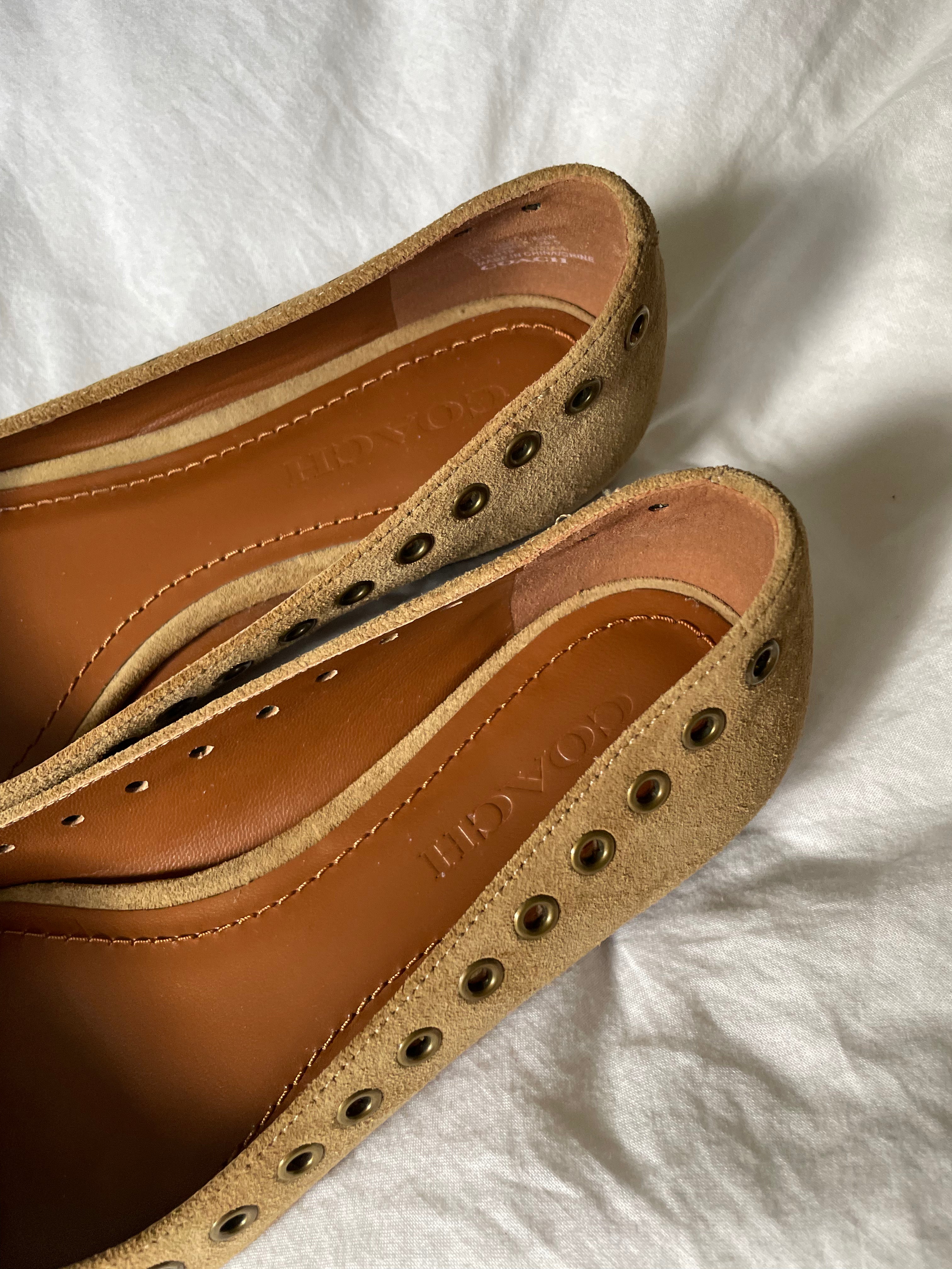 These vintage Coach ballet flats feature a pointed toe, lace-up details, and gold-tone eyelets along the edges. Crafted from beige suede with a smooth leather lining.