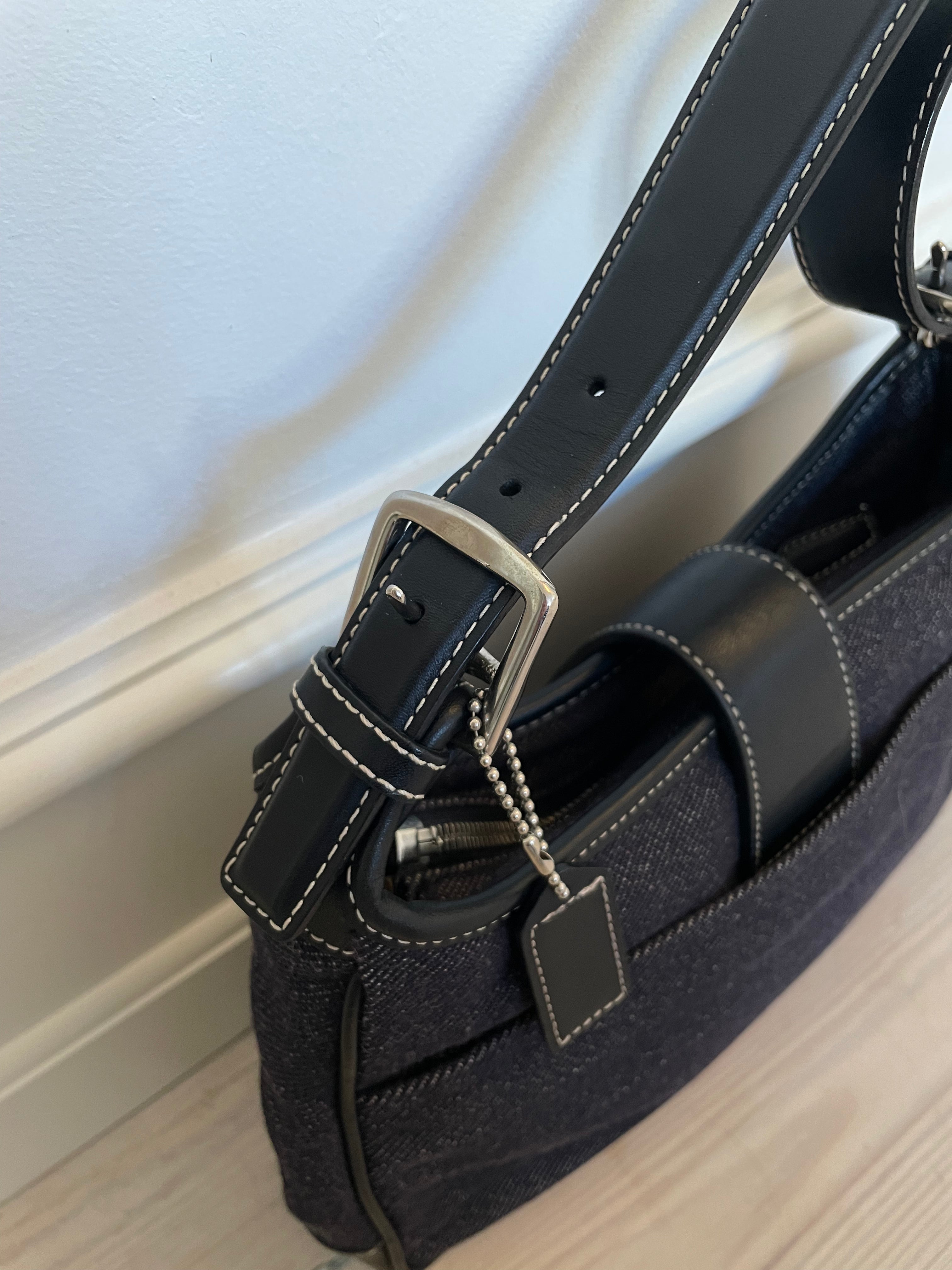 This vintage Coach bag from year 2000 is crafted from black leather and denim. It comes with an adjustable strap and magnetic closure, along with both an interior and exterior pocket. The bag is in great condition.